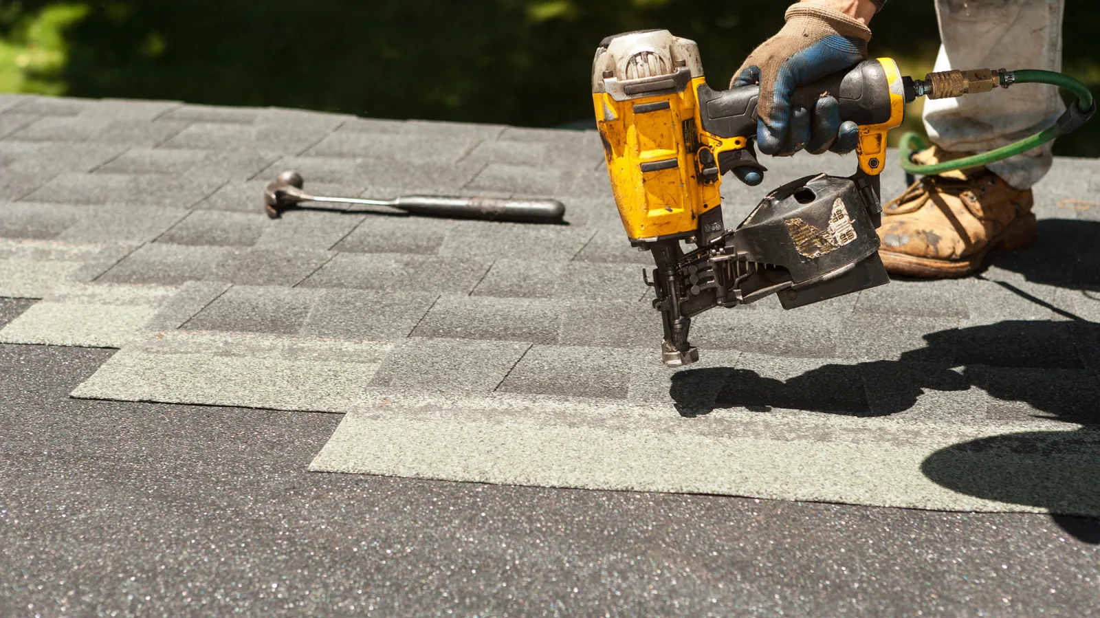 A roofer nailing shingles with a hammer resting nearby